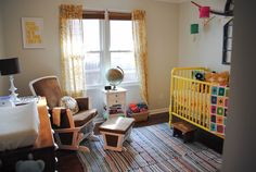 a baby's room with yellow crib, rocking chair, and colorful rug