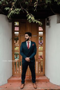 a man standing in front of a wooden door wearing a suit and tie with his hands on his hips