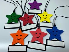 six colorful stars with faces are hanging from strings on a white surface, one has a name tag and the other has a smiling face