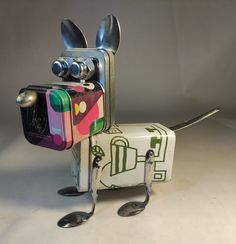 a metal dog with spoons and forks in it's mouth sitting next to a tin can