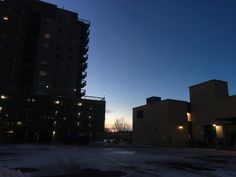 an empty parking lot at dusk with buildings in the background