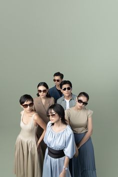 a group of people standing next to each other in front of a gray wall with sunglasses on