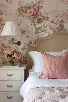 a white bed topped with pink flowers next to a night stand and lamp on top of a dresser