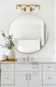 a white bathroom with a round mirror above the sink