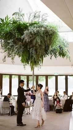 a man and woman dancing under a tree in a room with people sitting at tables