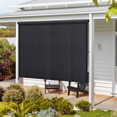 a black roller shade on the side of a house in front of some bushes and trees