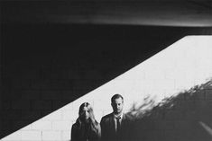 a man and woman standing next to each other in front of a white brick wall