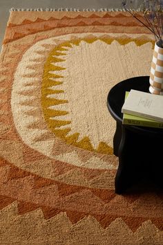 a table with a vase and books on top of it next to a rug that has an abstract design