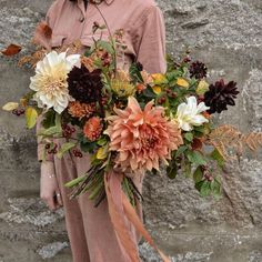 a woman holding a bouquet of flowers in front of a stone wall