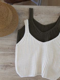 two knitted vests sitting on top of a wooden table next to a straw hat