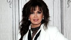 a woman with long hair wearing a white suit and black tie, posing for the camera