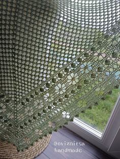 a green crocheted shawl hanging from the side of a window sill