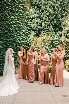 a group of women standing next to each other in front of a lush green wall