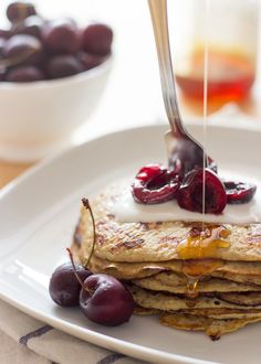 a plate with pancakes and cherries on it being drizzled with syrup