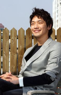 a young man sitting on top of a chair next to a wooden fence with buildings in the background