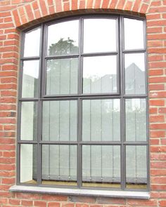 a cat sitting on the ledge of a brick building looking out an open window with bars