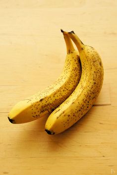 two ripe bananas sitting on top of a wooden table next to each other with black speckles