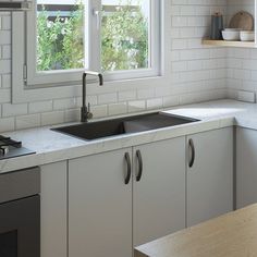 a kitchen with white tile walls and counter tops, two windows above the sink are open to let in natural light