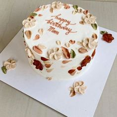 a white cake with flowers on it sitting on top of a card board next to some cookies