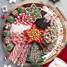 a wooden platter filled with christmas cookies, candy and candies on top of a table