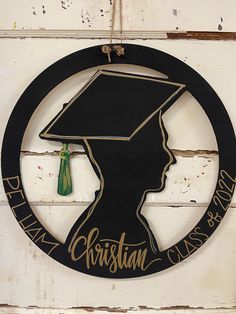 a black and gold graduation sign with a graduate's cap on it, hanging from the side of a white door