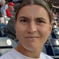 a woman is sitting in the stands at a baseball game and has her face close to the camera