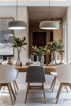 an elegant dining room with white chairs and wooden table surrounded by potted greenery