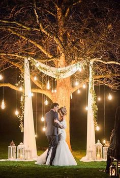 a bride and groom standing in front of a tree with lights strung from the branches