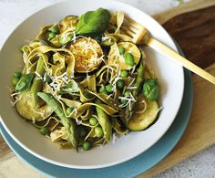 a white bowl filled with pasta and peas on top of a wooden cutting board next to a fork