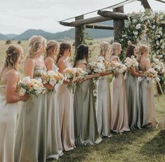 a group of women standing next to each other in front of a wooden structure holding bouquets