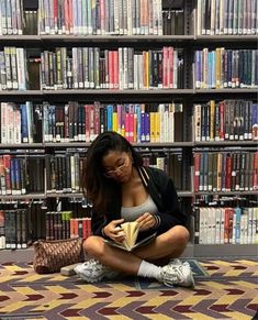 a woman sitting on the floor reading a book in front of a library full of books