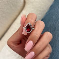 a woman's hand holding a ring with a red stone in the middle and diamonds around it