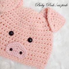 a crocheted pig hat with black eyes and nose is laying on a white blanket