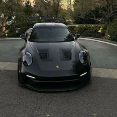 a black sports car parked in front of a driveway with trees and bushes behind it