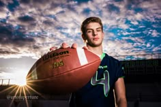 a young man holding a football in front of a stadium with the sun behind him