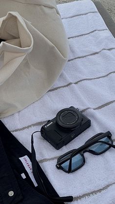 an open umbrella, sunglasses, and camera sitting on top of a towel next to a bag