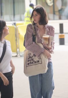 a woman is walking down the street carrying a bag and talking to another woman with her handbag