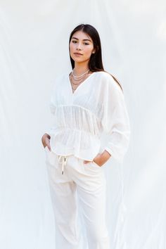 a woman standing in front of a white backdrop wearing pants and a top with ruffles