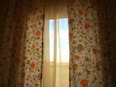 an open window with floral curtains in front of the grass and blue sky behind it