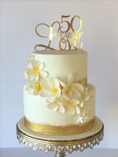 a white and gold 50th birthday cake with flowers on the top tier is shown in front of a white background