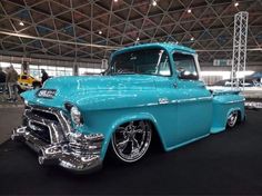 an old blue truck is parked in a showroom with other cars and people around it