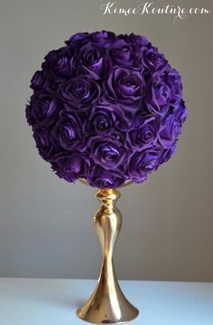 a gold vase filled with purple flowers on top of a white tablecloth covered table