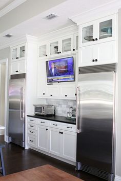 a kitchen with white cabinets and stainless steel appliances, including a flat screen tv on the wall