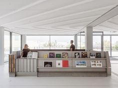 two people sitting on a couch in an empty room with large windows and lots of books