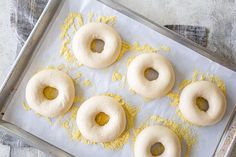 four doughnuts sitting on top of a baking sheet covered in yellow powdered sugar