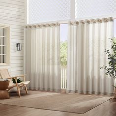 a living room with white curtains and a chair in front of the window that is open