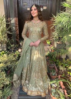 a woman standing in front of some plants wearing a green and gold lehenga