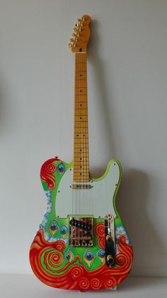 a green and red guitar sitting on top of a white wall