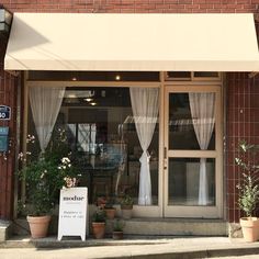 a store front with an awning over the door and flowers in pots on the sidewalk