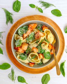 a bowl filled with pasta and spinach on top of a wooden plate next to green leaves